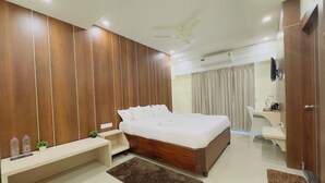A modern bedroom with a large bed, bedside tables, a desk, and a ceiling fan. - CITY GRAND (Puri)
