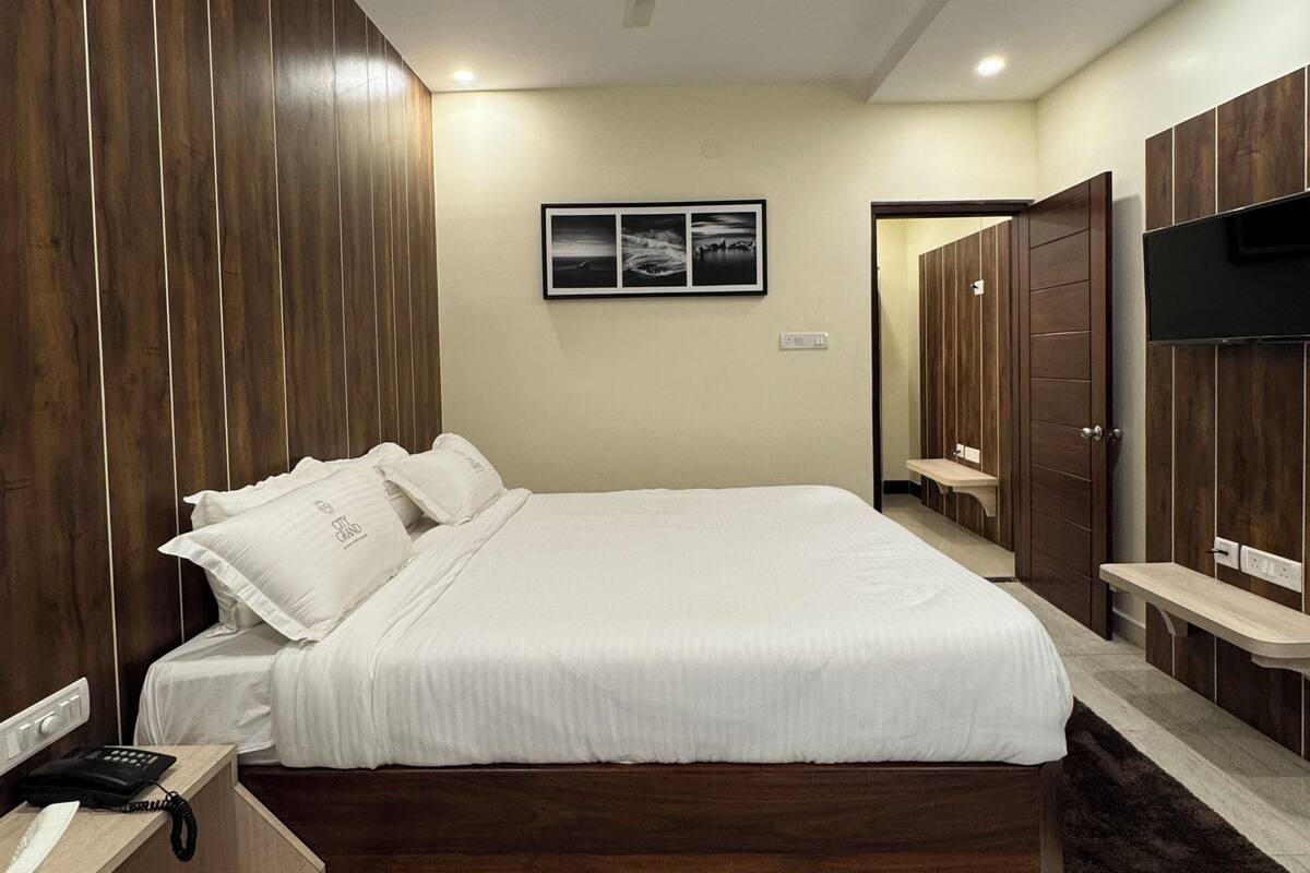 A modern bedroom with a wooden bed, a bedside table with a phone, a ceiling fan, and a wall-mounted TV.