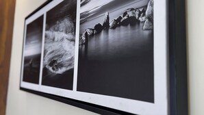 A framed photograph of a coastal scene with waves and rocks on a wall. - CITY GRAND (Puri)