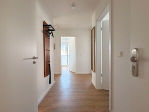 Un couloir doté d’un plancher en bois, de murs blancs et d’une porte munie d’une poignée moderne.