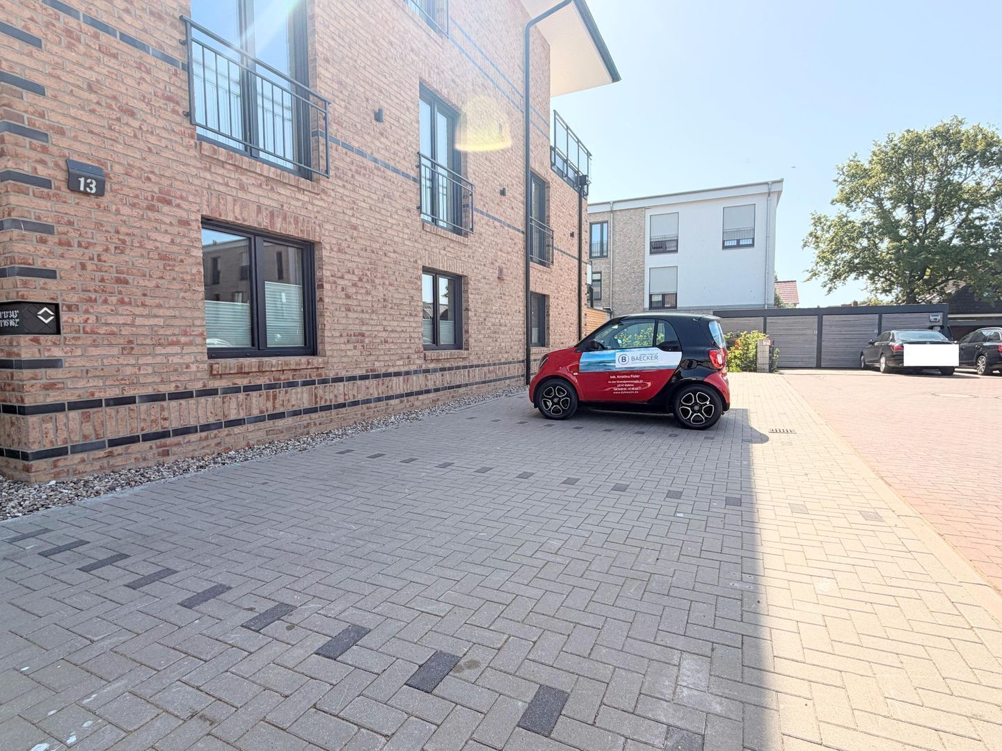 A small red car parked in front of a brick building with numbered windows and a paved walkway.