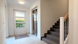 Ein Flur mit Tür, Fußmatte, Treppe und einer Wandlifteinrichtung.