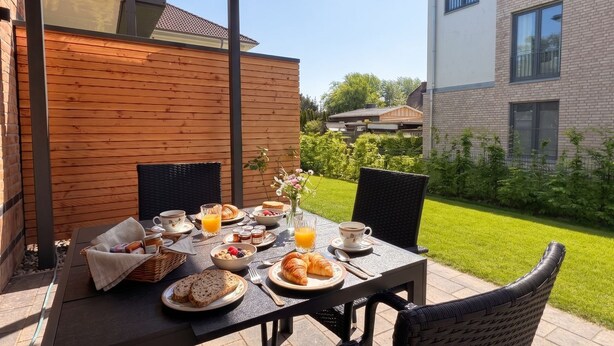 An outdoor dining area with a table set for breakfast, including croissants, fruit, and beverages. - 2120 - Gode Ström Quartiere "Twee" - Beach meadow - 2120 - Gode Ström Quartiere (Dahme)