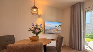 A modern dining area with a wooden table, two chairs, a vase of flowers, a hanging light fixture, and a beach scene on the wall. - 2120 - Gode Ström Quartiere "Twee" - Beach meadow - 2120 - Gode Ström Quartiere (Dahme)