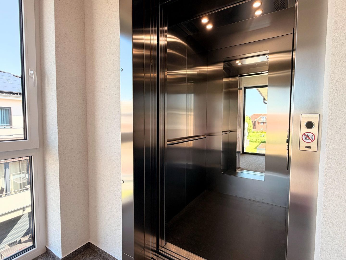 A modern elevator with stainless steel doors, a glass panel, and a no-smoking sign.