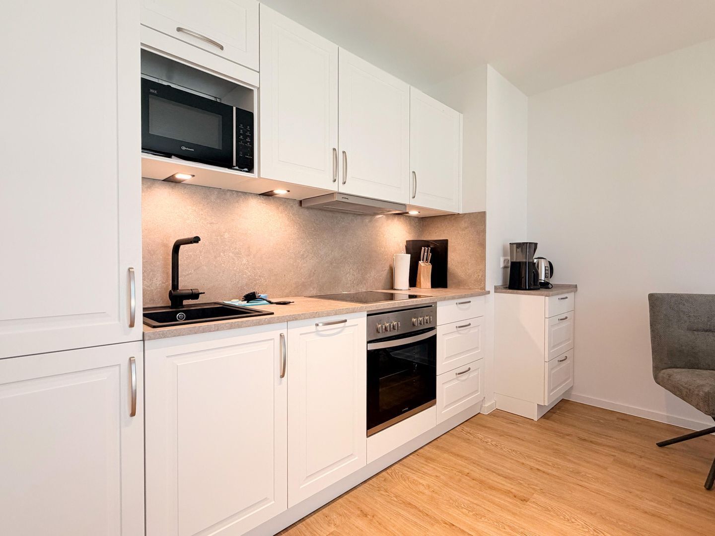 A compact kitchen with white cabinets, a microwave, a coffee maker, and a toaster.