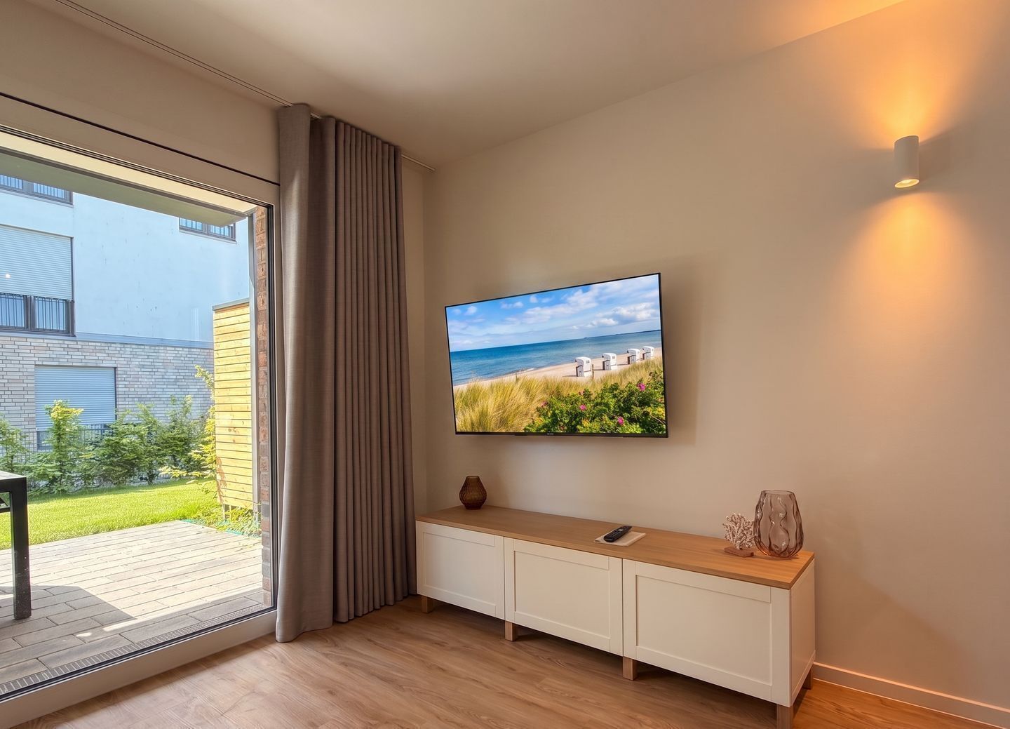 Un intérieur moderne avec une grande fenêtre, un téléviseur à écran plat, une console en bois et un luminaire fixé au mur.