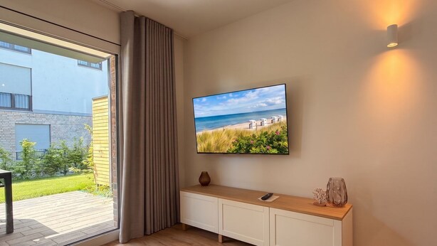 Ein modernes Interieur mit großem Fenster, Flachbildfernseher, Holzkonsole und Wandleuchte.