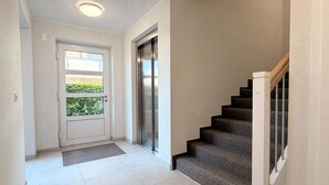 Ein Flur mit Tür, Fußmatte, Treppe und einer Wandlifteinrichtung.