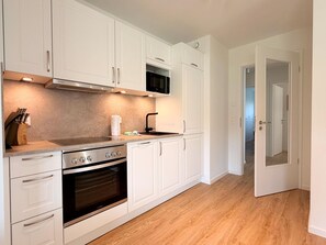A kitchen with white cabinets, a stove, oven, and a microwave. - 2130 - Gode Ström Quartiere "Dree" - Beach meadow - 2130 - Gode Ström Quartiere (Dahme)