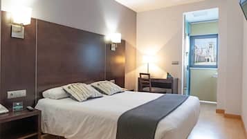 Habitación de hotel con una cama grande, lámparas de noche, un escritorio y vista a un edificio desde la puerta.