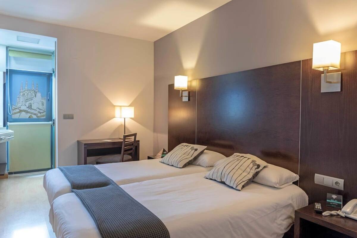 A hotel room with two beds, a desk, a chair, and a nightstand with a phone.