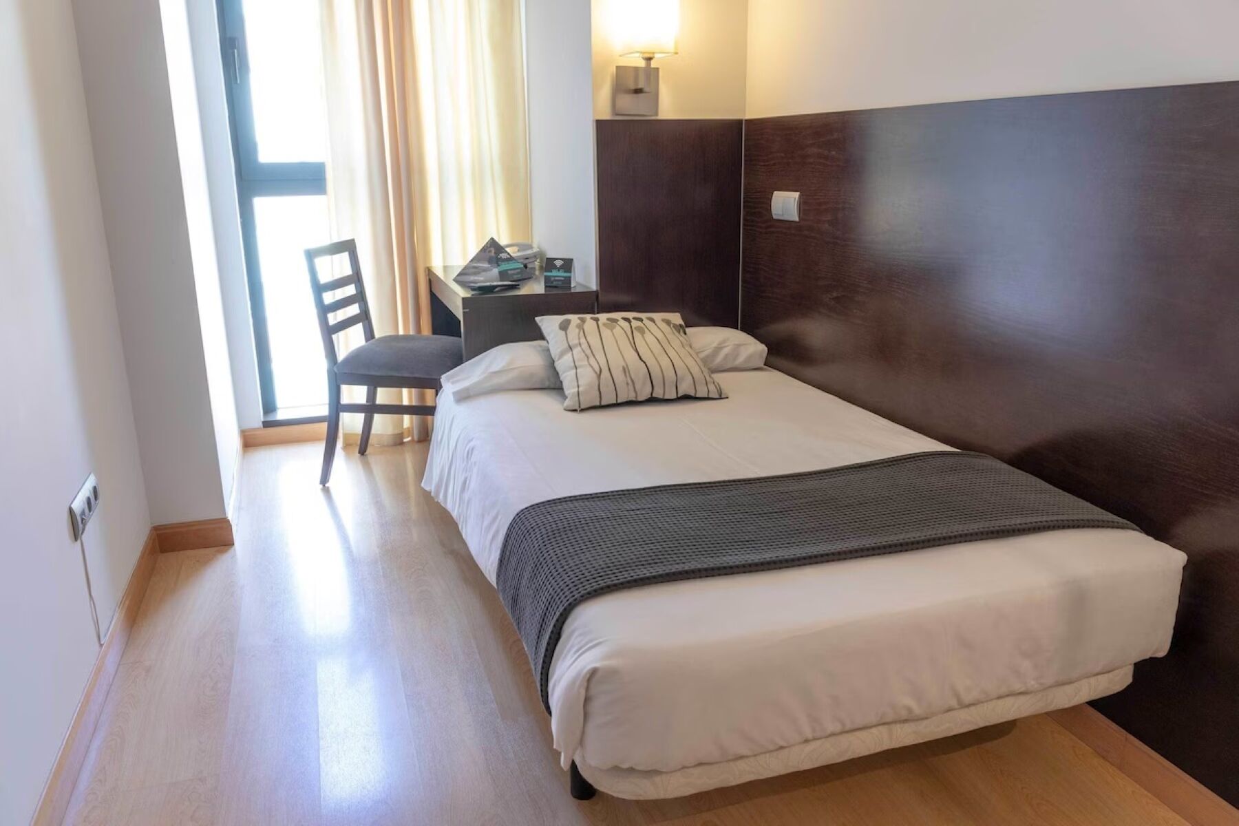 A hotel room with a bed, a chair, a desk, and a lamp.