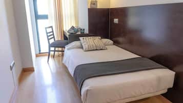 Una habitación de hotel con cama, una silla, un escritorio y una lámpara.