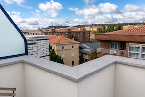 Un edificio residencial con balcón en esquina, fachada de ladrillo y vistas a otros edificios e iglesia al fondo.