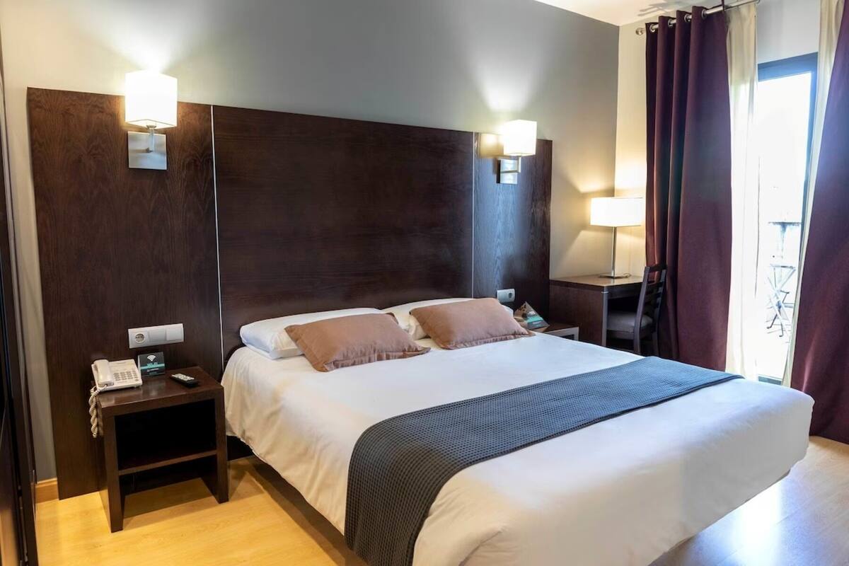 A hotel room with a large bed, two bedside tables, a desk, and a chair.