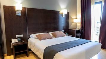 Una habitación de hotel con una cama grande, dos mesitas de noche, un escritorio y una silla.