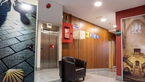 A lobby with a wooden wall, a black leather chair, an elevator, and a staircase.