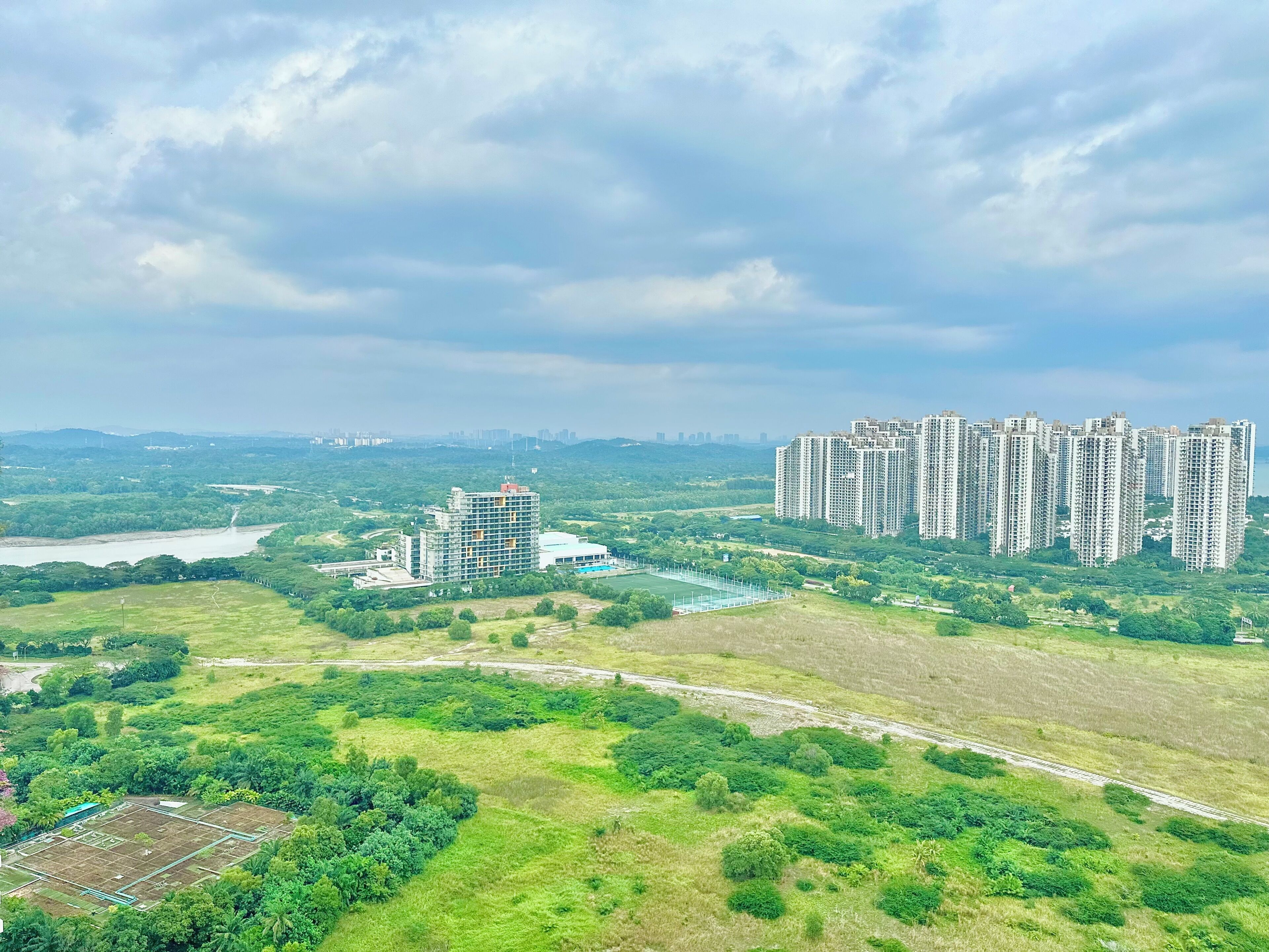 A high-rise residential building complex with multiple apartment towers, surrounded by green fields and a river.