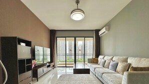 Una sala moderna con sofá, reposapiés, televisor y mueble de entretenimiento.