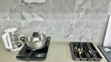 A kitchen with a gas stove, a pot on the stove, a kettle, and a utensil holder.