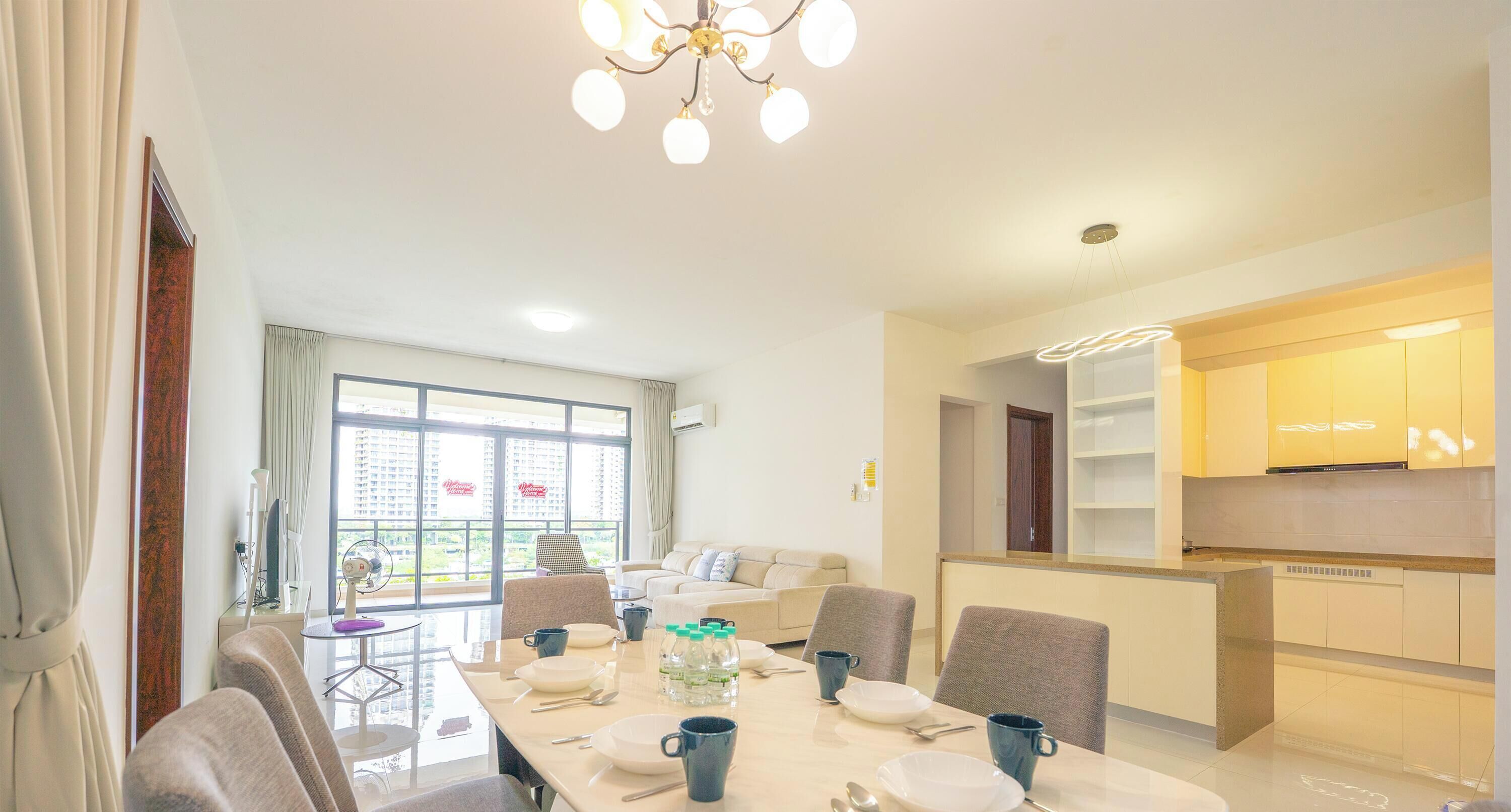 A modern dining area with a long table set for four, a sofa, and a kitchen area with cabinets and a microwave.