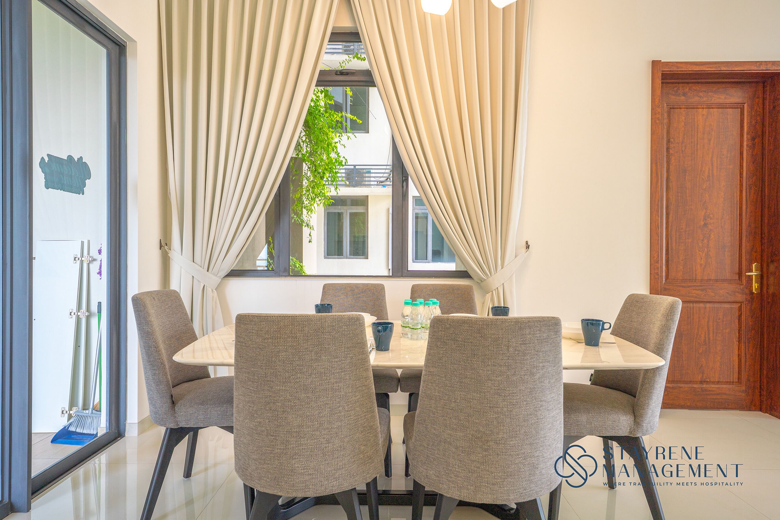 A dining area with a table and chairs, a window with curtains, and a wooden door.