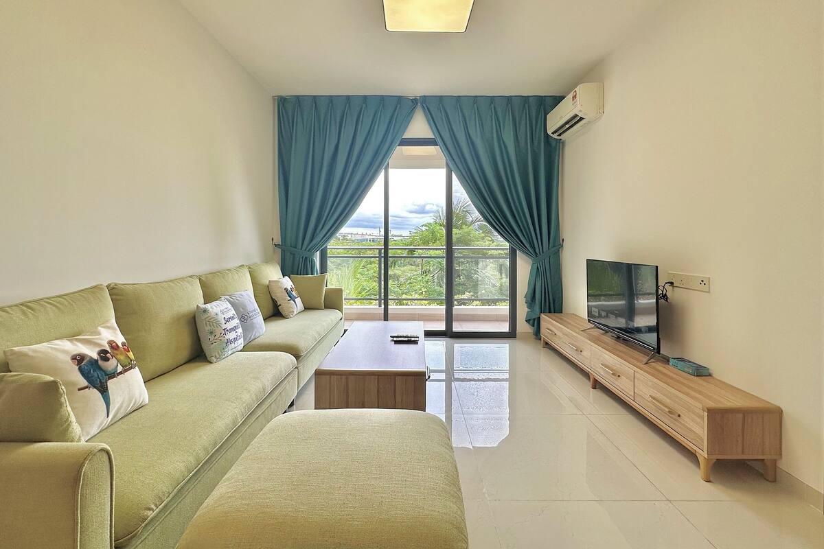 Un salon moderne avec un canapé, une table basse, un téléviseur et une vue sur la verdure grâce à de grandes fenêtres.