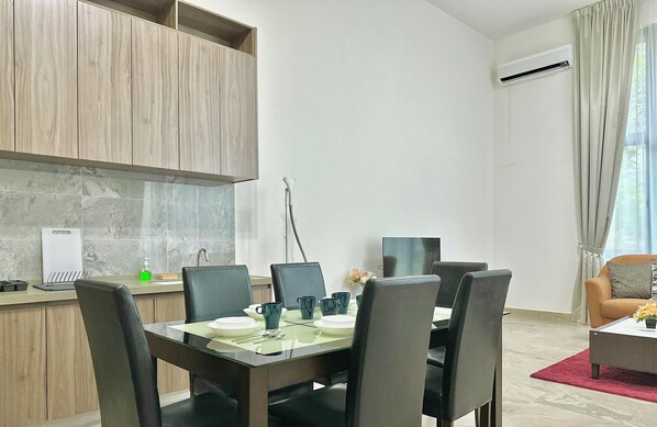 A modern kitchen with wooden cabinets, a marble countertop, and a dining area with a glass table and black chairs. - Casa Forest City JB by Stayrene (Gelang Patah)