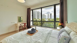 Un dormitorio con un ventanal grande, una cama con almohadas, una mesita de noche, un escritorio y una silla.