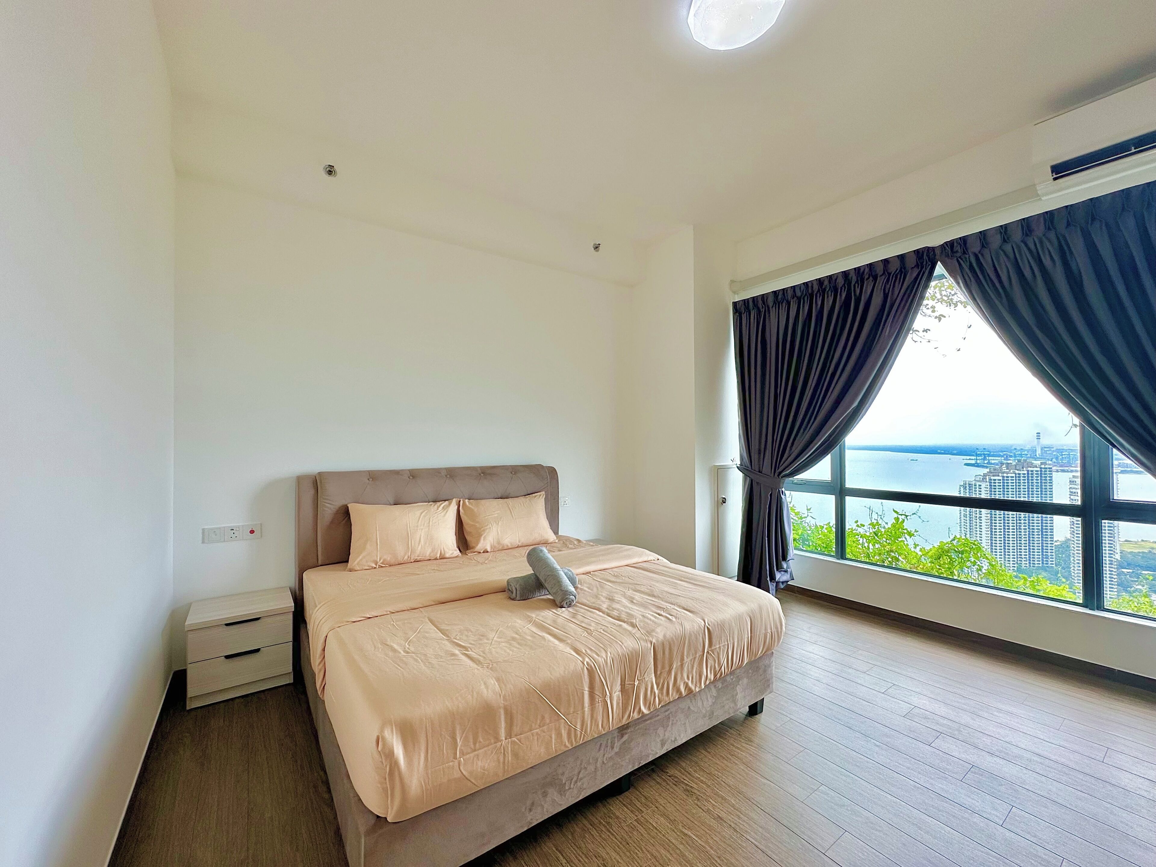 Un dormitorio con cama, mesita de noche, ventana con cortinas y vista a la ciudad.