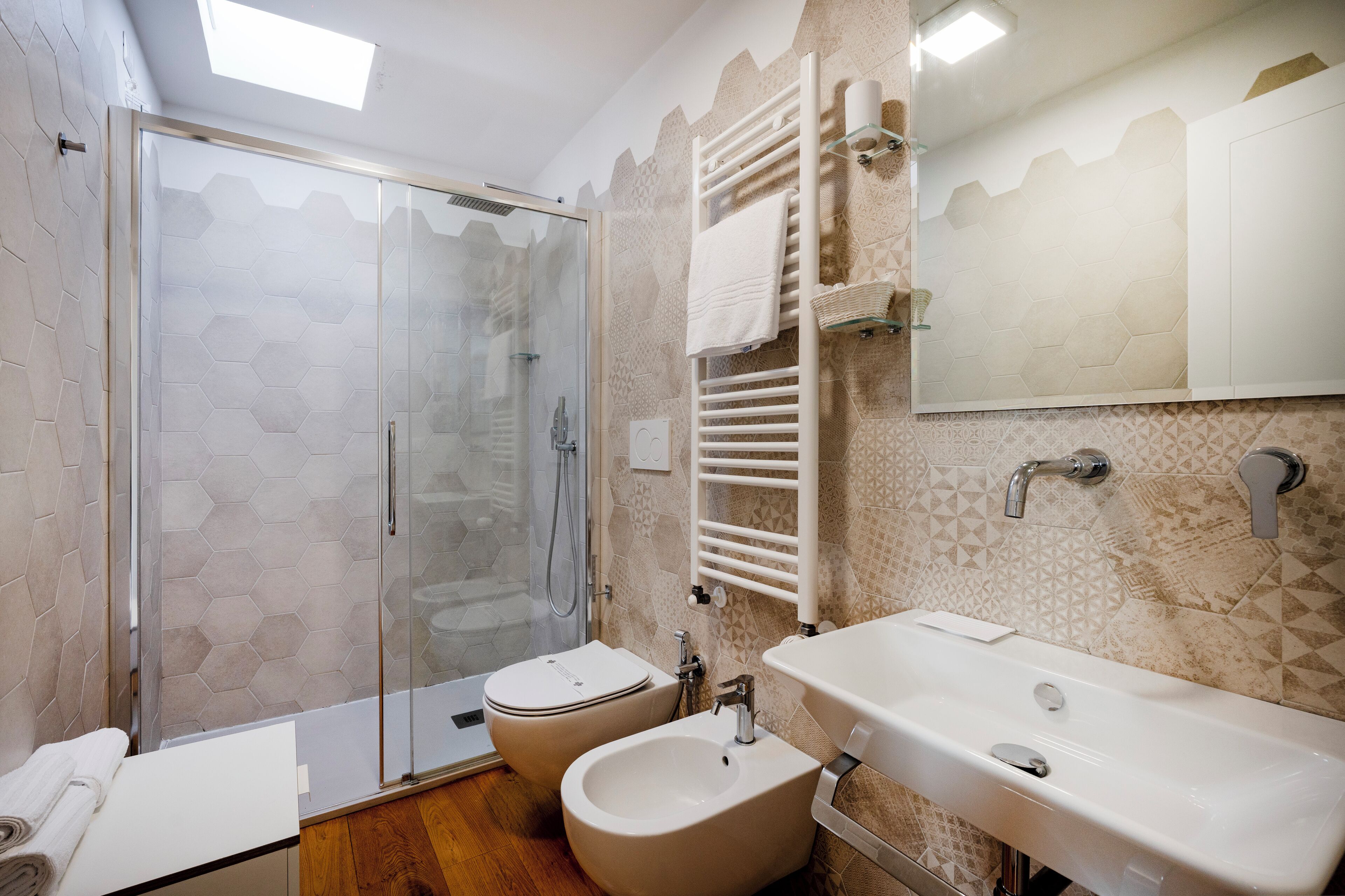 A modern bathroom with a glass shower enclosure, a bidet, a sink, and a towel rack.