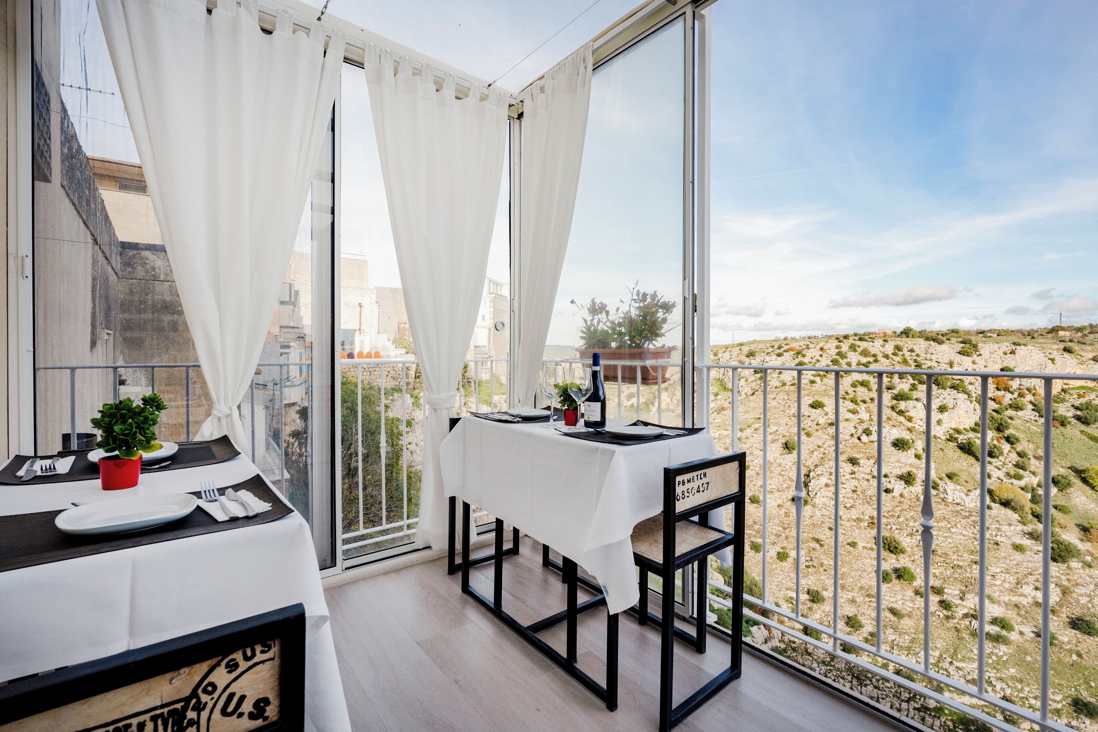 Un balcone con tavolo apparecchiato per mangiare, una sedia e vista su un paesaggio collinare.