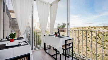 Un balcone con tavolo apparecchiato per mangiare, una sedia e vista su un paesaggio collinare.