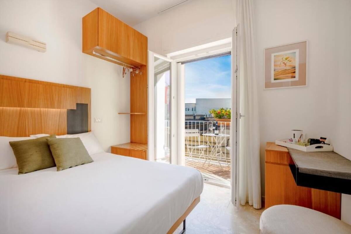 Habitación de hotel con cama, escritorio, una silla y balcón con vistas.