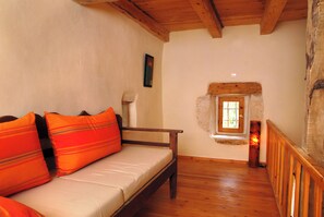 Ein Sofa mit Holzrahmen und orangenen Kissen in einem Raum mit Holzböden und einer Steinwand.