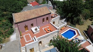 Ein zweistöckiges Gebäude mit einem Ziegeldach, einem Pool und Sitzgelegenheiten im Freien.