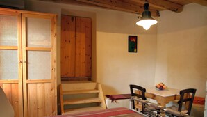 Ein Schlafzimmer mit einem Bett, einem Holzschrank, einem Esstisch mit Stühlen und einer Treppe.