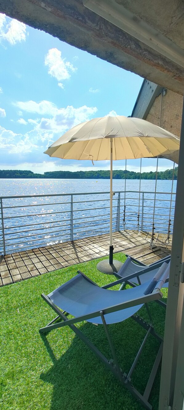 A deck with a view of a lake, a lounge chair, and a large umbrella.