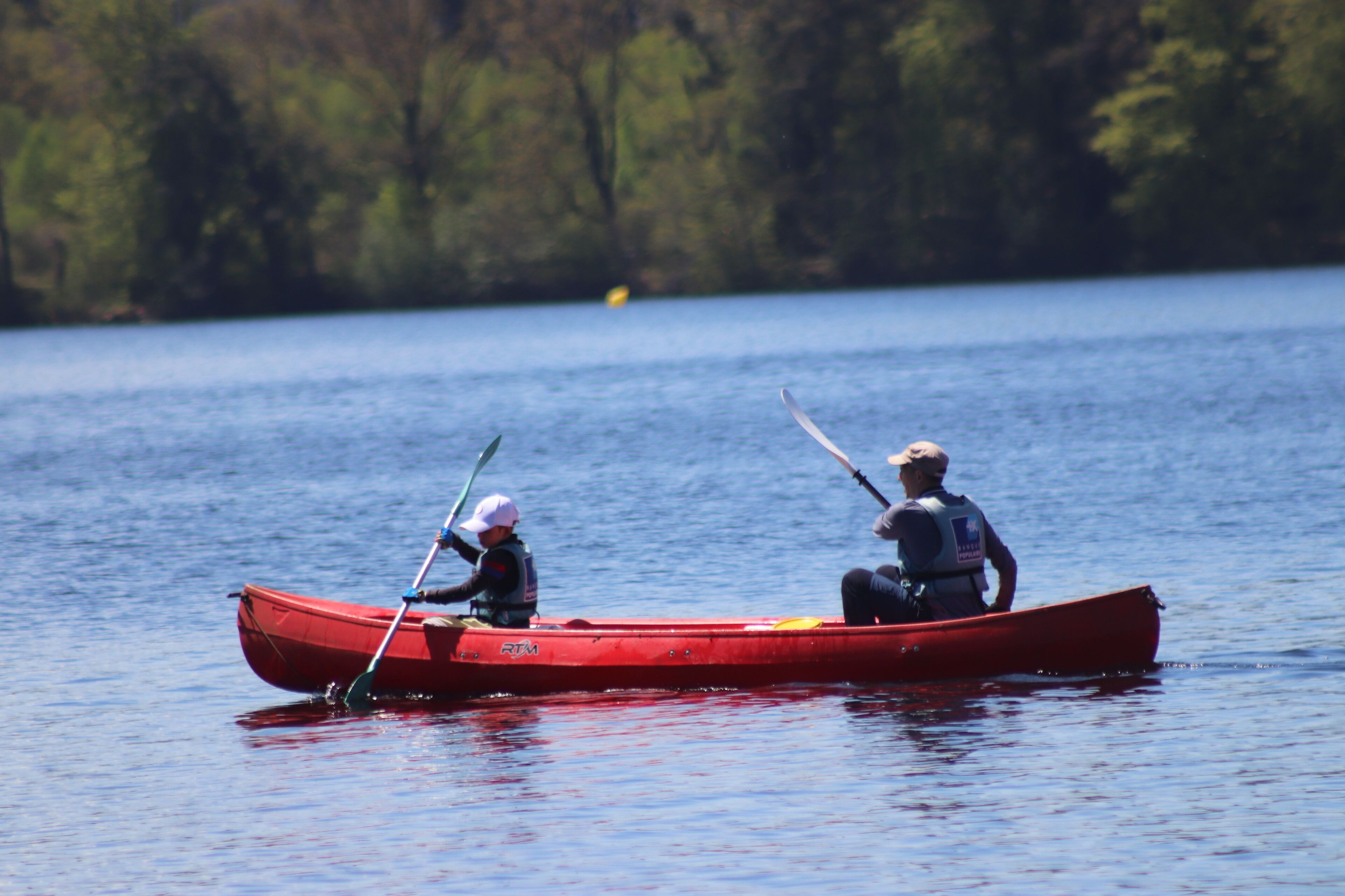 Un canoë rouge sur une eau calme, avec deux personnes qui pagayent.