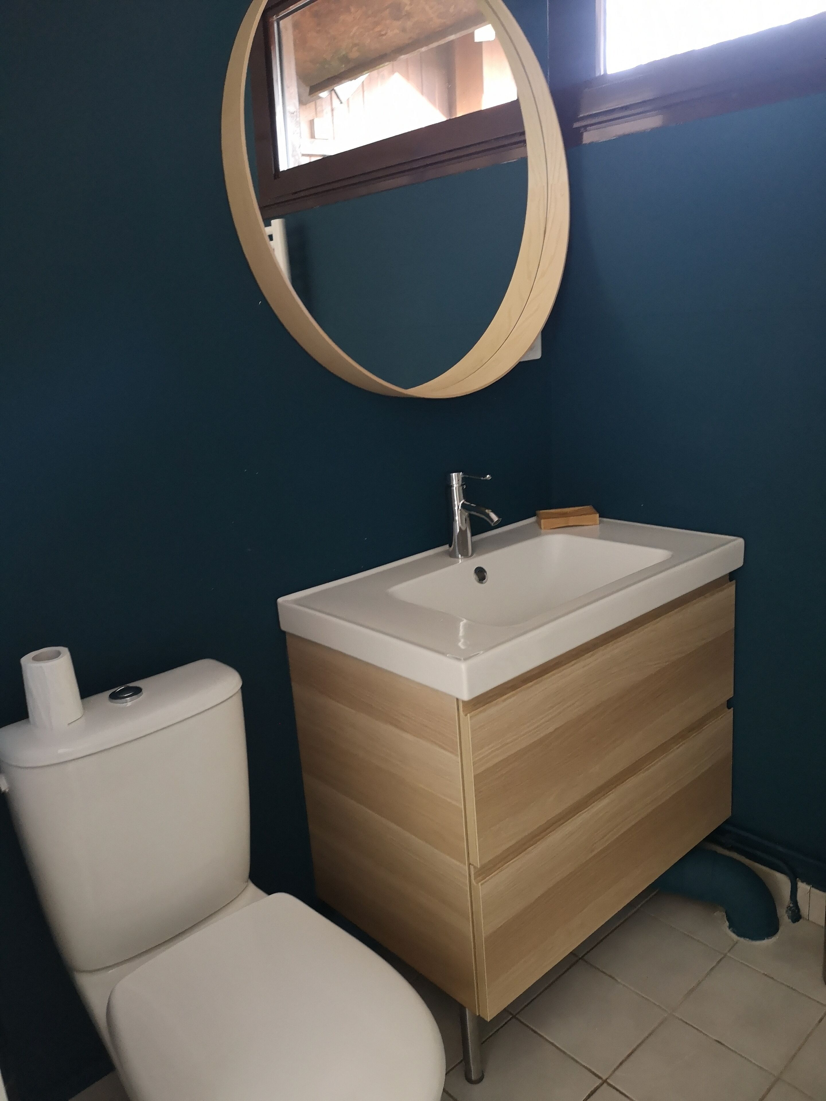 Ein Badezimmer mit Toilette, einem Waschbecken mit Holzschrank und einem runden Spiegel an der Wand.