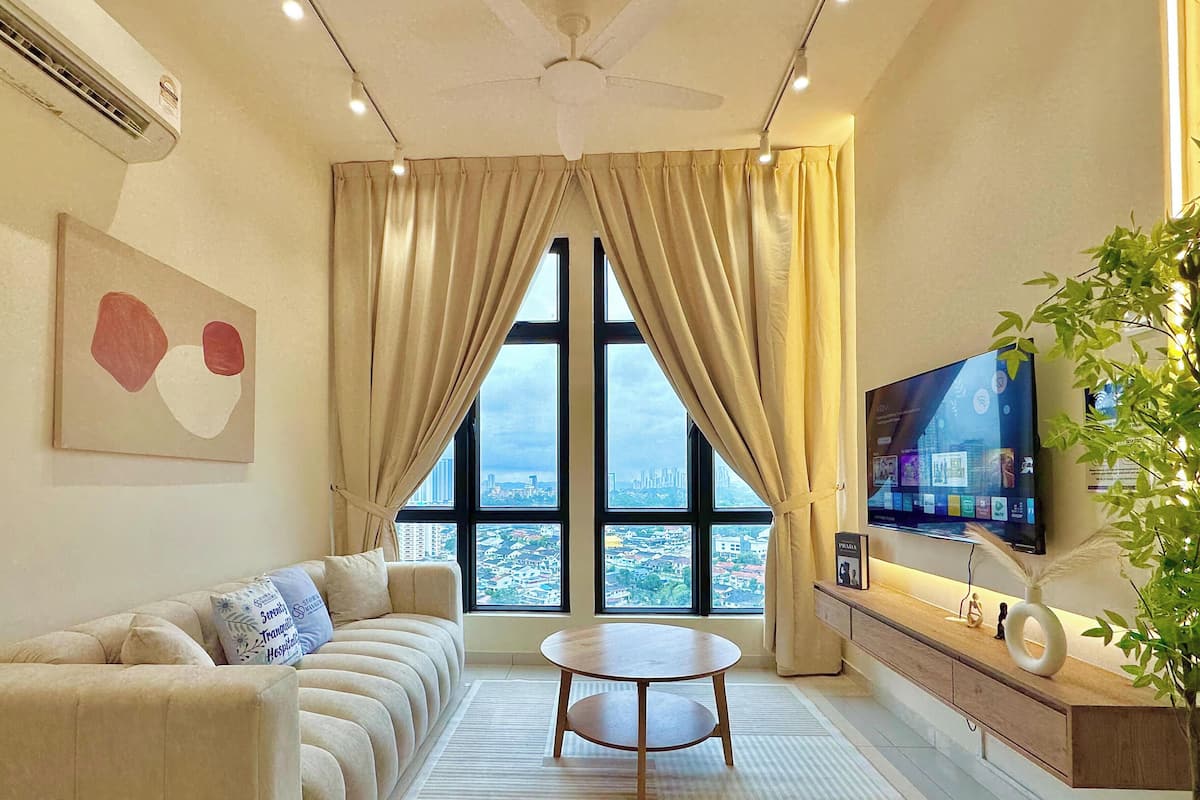 A modern living room with a sofa, a round table, a TV, and a large window with curtains.