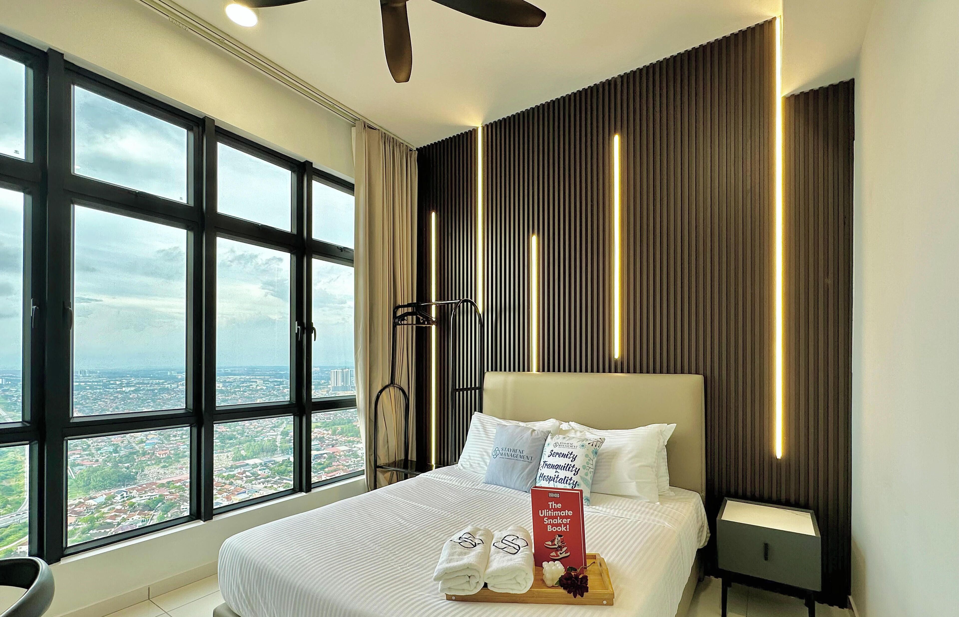 A hotel room with a large window, a bed with white bedding, a bedside table, and a ceiling fan.