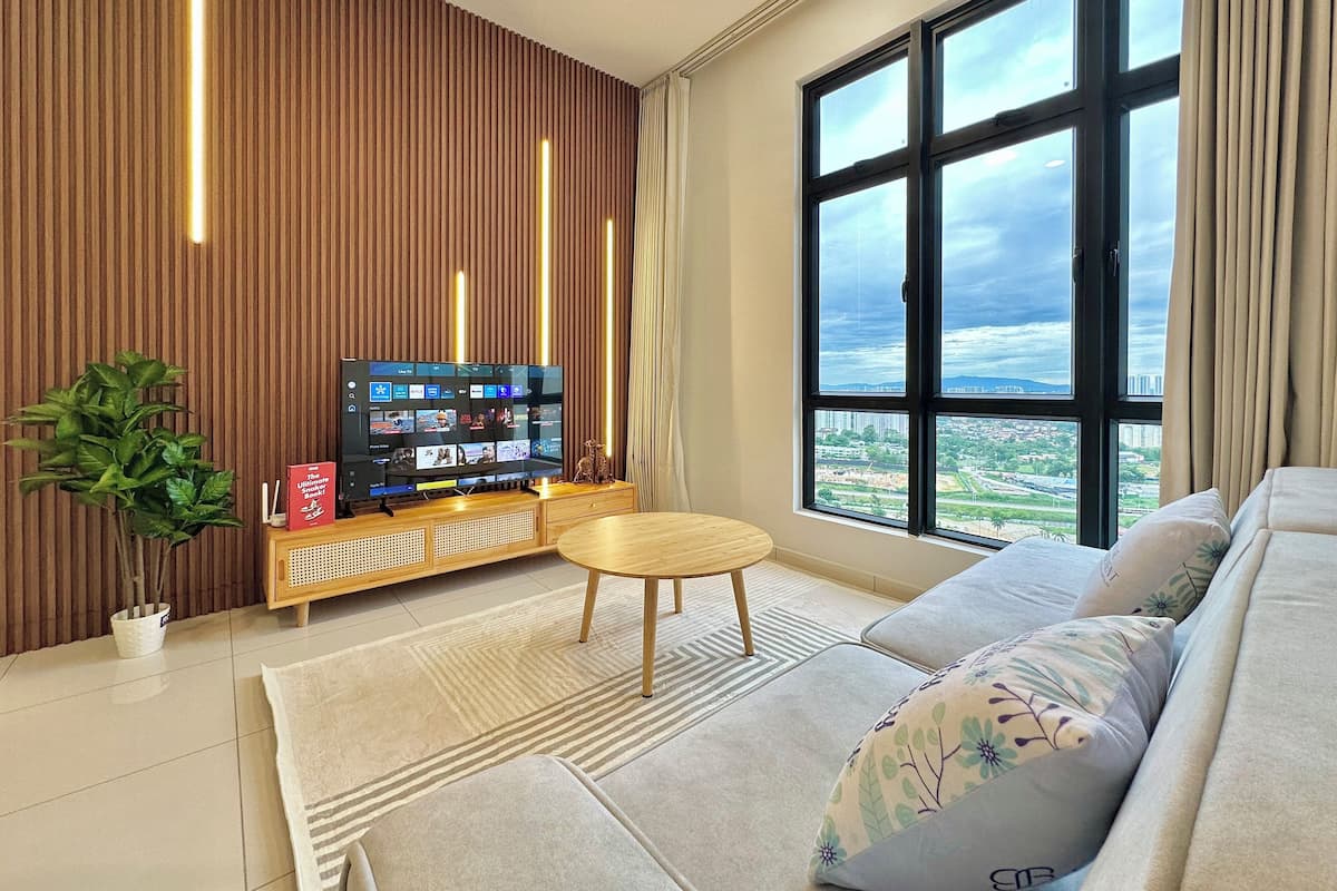 A modern living room with a flat-screen TV, a sofa, a small round table, and a large window offering a city view.