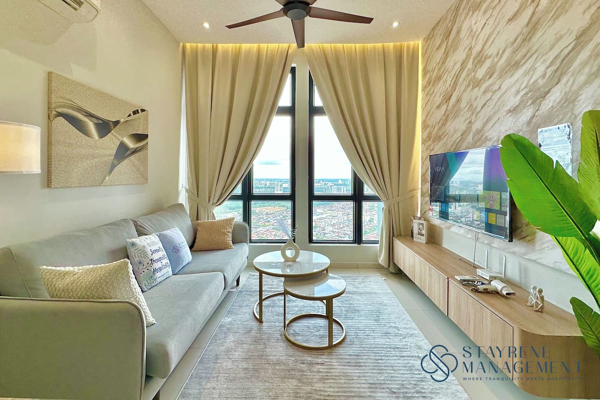 A modern hotel room with a sofa, a small round table, a ceiling fan, a TV, and a large window with curtains.