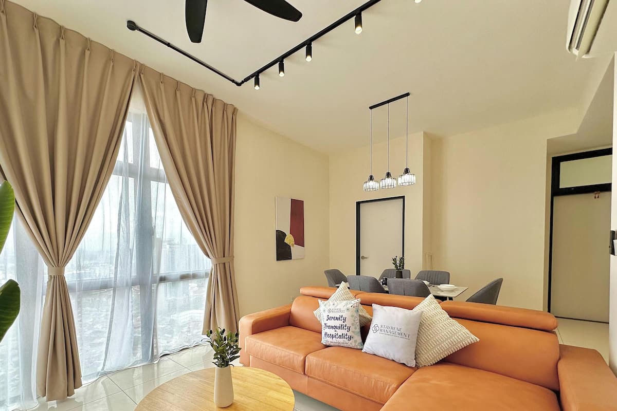 A modern living room with a sofa, a dining table, and a large window with curtains.