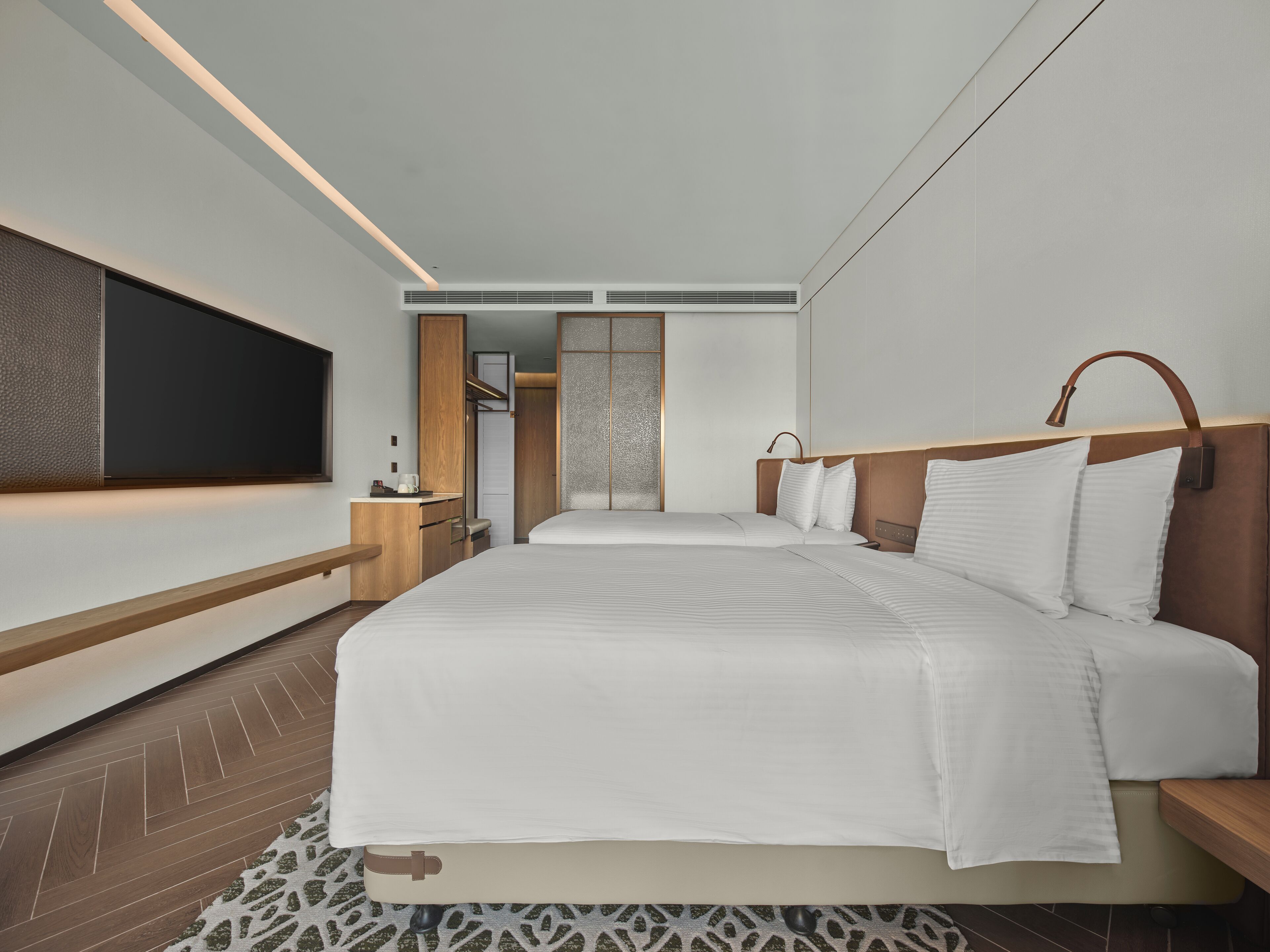 Una habitación de hotel moderna con una cama grande, un televisor montado en la pared y un vestidor.