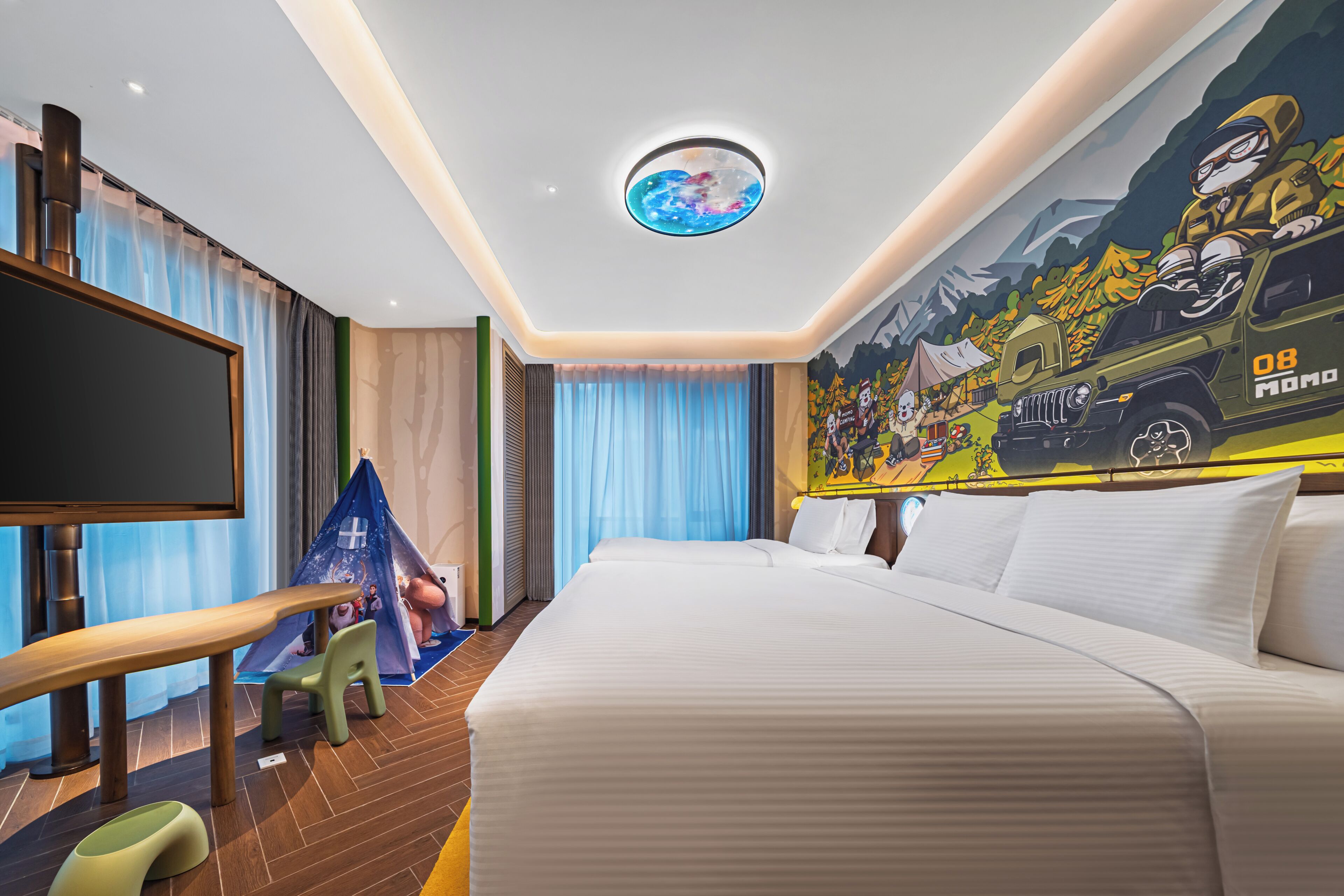 Habitación de hotel con una cama grande, televisión de pantalla plana, un rincón de juegos pequeño y un mural en la pared.