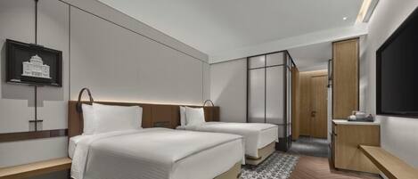 Ein modernes Hotelzimmer mit zwei Betten, einem Schreibtisch, einem Fernseher und einem gerahmten Bild an der Wand.