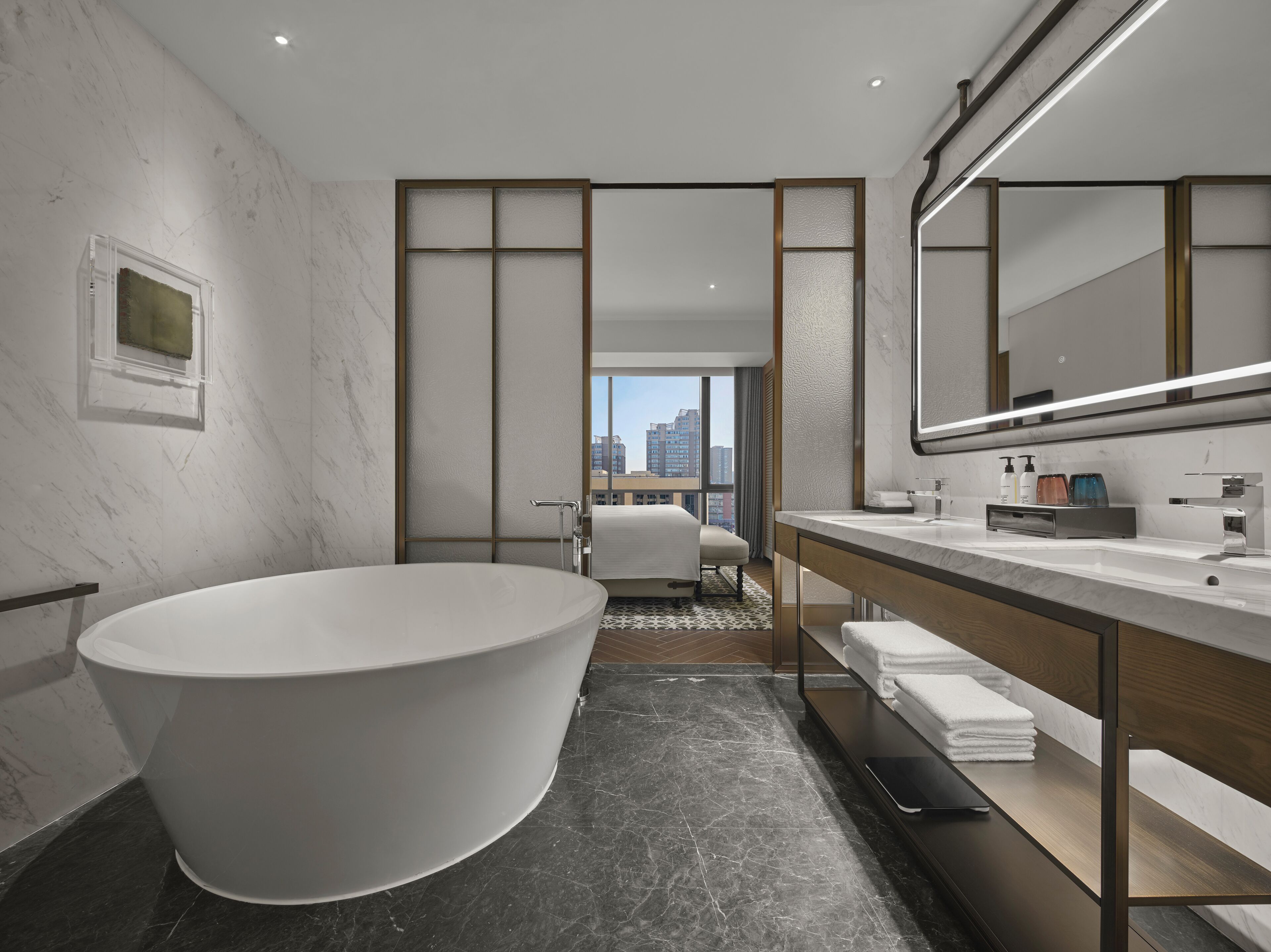 Un baño moderno con una bañera grande, un tocador con espejo y vistas a la ciudad a través de un ventanal.